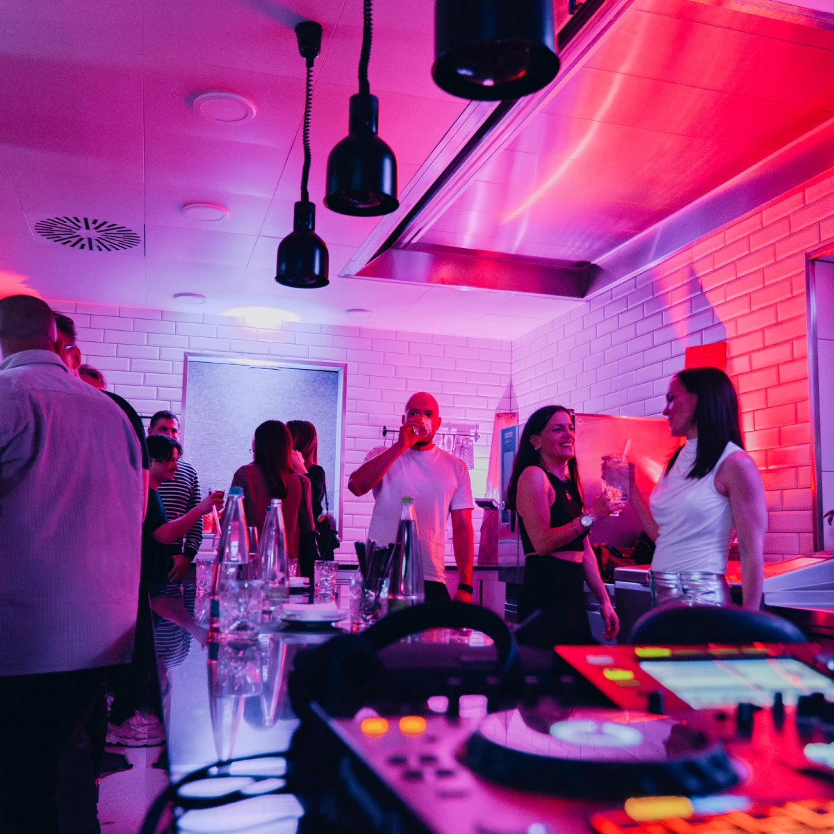 Eventk&uuml;che mit G&auml;sten, Drinks und DJ-Equipment im Hintergrund.