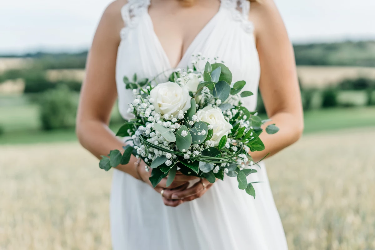 Braut mit Blumenstrauß im Grünen.