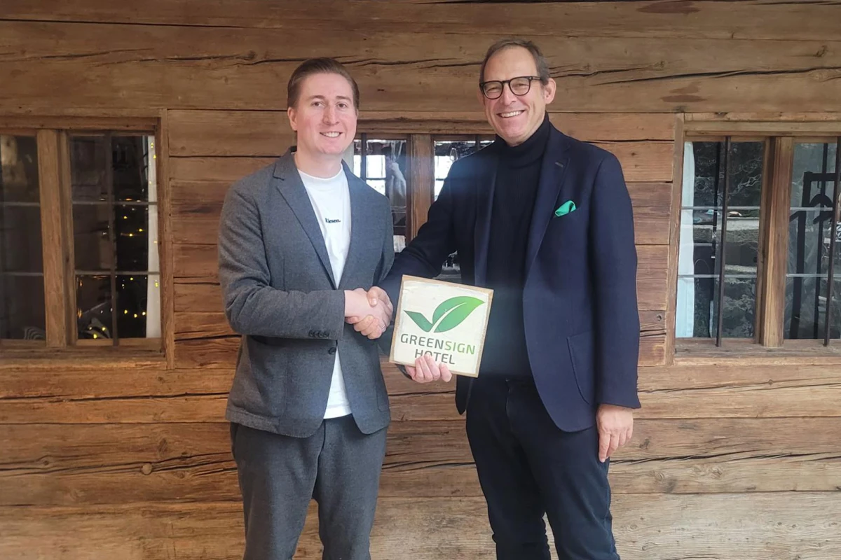 Philipp Schneider vom Hotel Riesengebirge (links) und Roberto Pareras von GreenSign (rechts) geben sich die H&auml;nde und l&auml;cheln in die Kamera. In der Hand h&auml;lt Philipp Schneider ein Schild mit der Aufschrift "Green Sign Hotel".
