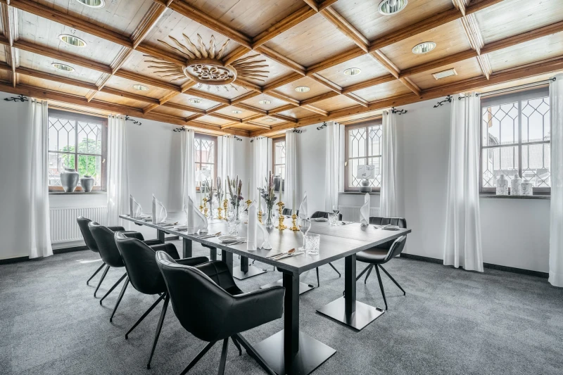 Moderner Konferenzraum mit gro&szlig;en Fenstern und Holzdecke. Langer wei&szlig;er Tisch mit schwarzen Designerst&uuml;hlen, dekoriert mit Vasen und Kerzen. Helle, elegante Atmosph&auml;re mit nat&uuml;rlichem Tageslicht.